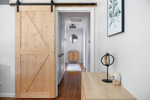 A hallway with a wooden sliding door, a small cabinet, a mirror, and a framed botanical print on the wall.