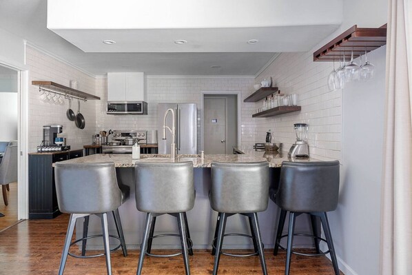 A modern kitchen with white subway tiles, stainless steel appliances, and a bar area with four stools.