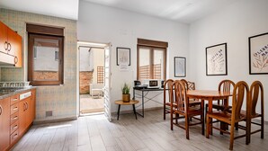 A modern kitchen with wooden cabinets, a dining table with chairs, and a small side table with a plant. - Holiday Home 'Little Yellow House' with Private Terrace (Gijón)