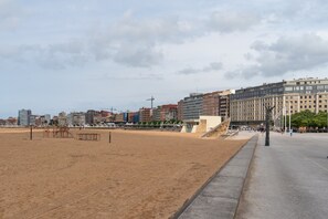 En sandstrand med by i baggrunden, inklusive bygninger og en kran.