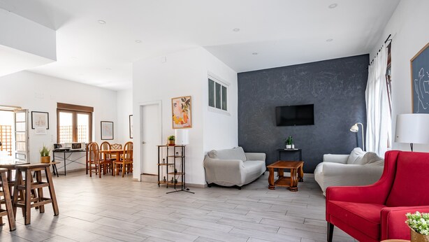 A spacious living area with a dining set, two sofas, a red armchair, and a flat-screen TV mounted on a dark wall. - Holiday Home 'Little Yellow House' with Private Terrace (Gijón)