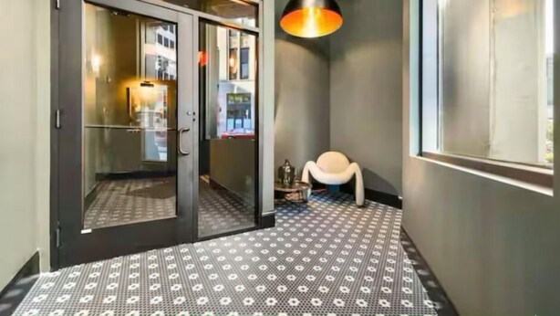 A hallway with patterned flooring, a door with glass panels, a hanging pendant light, and a chair.