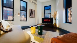 A modern living room with a large window, a flat-screen TV, and a cozy seating area.