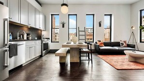 Una cocina moderna con armarios blancos, una zona de comedor con mesa de madera y un sofá negro.