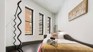 Una habitación de hotel con una cama, una alfombra roja, una silla negra y una escultura de metal negro.
