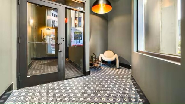 Un pasillo con piso estampado, una puerta que da a una habitación y un candelabro colgante.