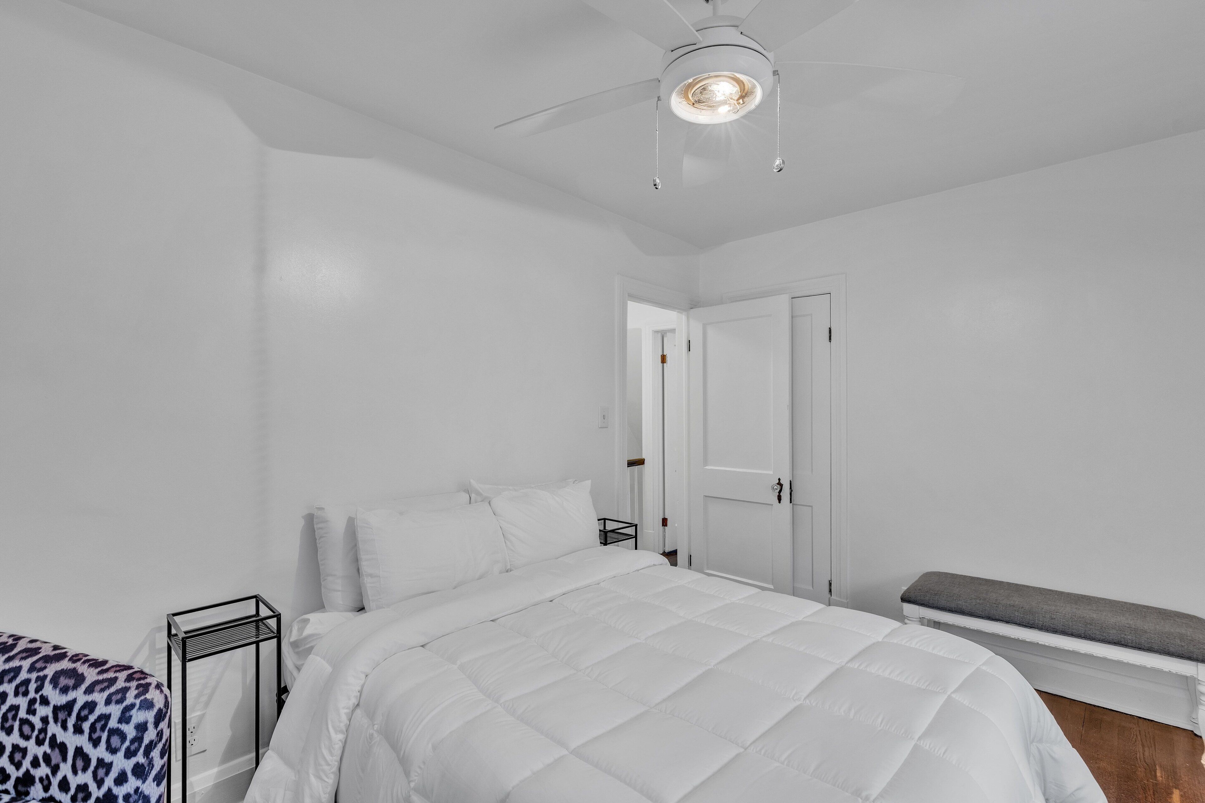 Une chambre à coucher comprenant un lit, un banc, une table de chevet et un ventilateur de plafond.