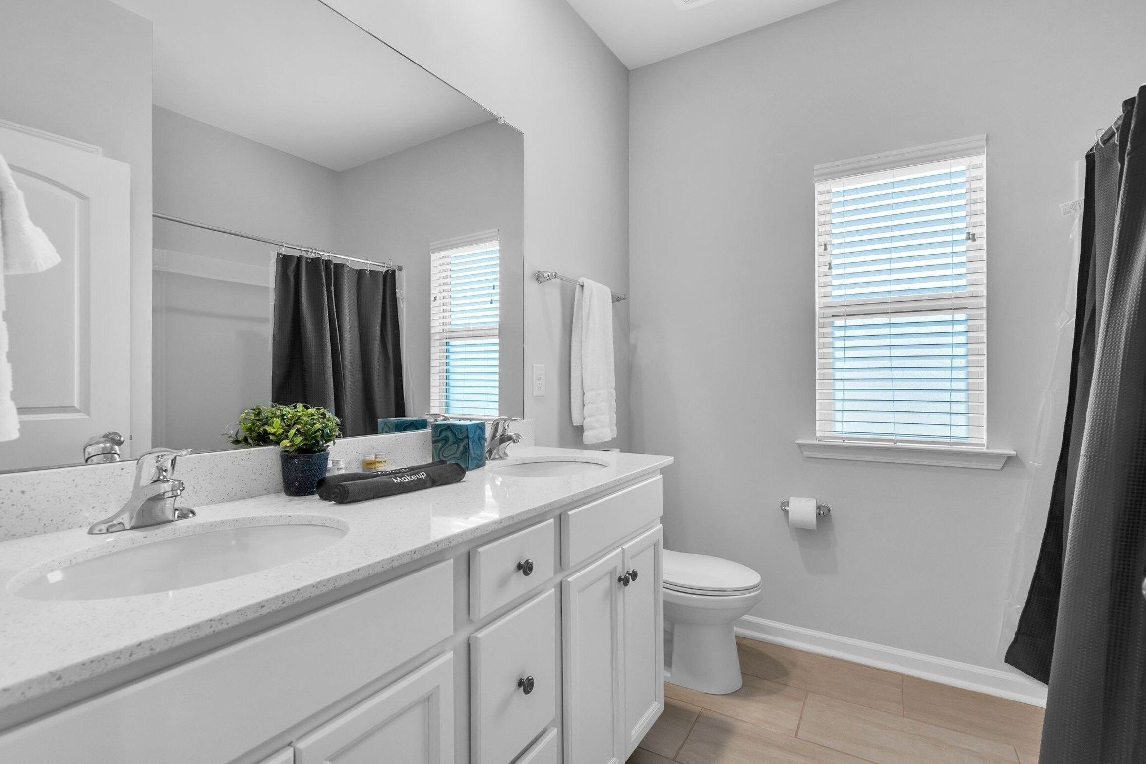 A modern bathroom with two sinks, a large mirror, and a toilet. There are towels hanging on the wall and a shower curtain.