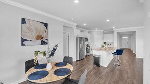 Una cucina moderna con elettrodomestici in acciaio inossidabile, una zona pranzo con un tavolo rotondo in legno e un soggiorno con un grande quadro floreale.
