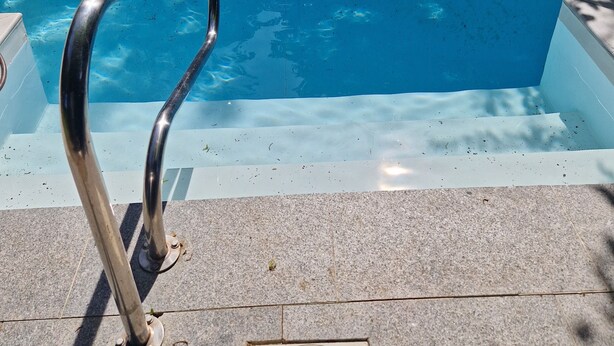 Une piscine avec un escalier en métal et un couvercle de regard situé sur le bord.