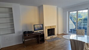Un salon avec une cheminée, un téléviseur posé sur un meuble, une table à manger et une vue sur un balcon doté d’une balustrade.