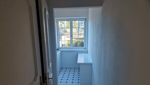 Un couloir étroit avec une fenêtre au fond, un sol carrelé et une porte sur la gauche.