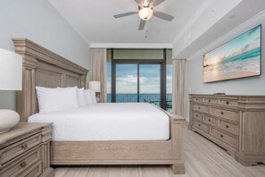A bedroom with a large bed, a ceiling fan, a view of the ocean, and a wooden dresser. - Phoenix Gulf Shores Ii 2304 3 Bedroom Condo (Gulf Shores)