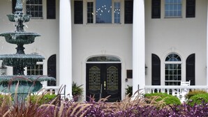 A building with a central entrance, a fountain, and a well-maintained garden with purple and white flowers. - 2909 2 Bedroom Villa (Calabash)