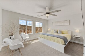 A bedroom with a bed, two windows, a ceiling fan, a bedside table, and a chair. - Forever Summer 5 Bedroom Townhouse (Washington)