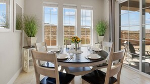Un espace repas comprenant une table ronde, des chaises et offrant une vue sur un paysage désertique grâce à de grandes fenêtres.