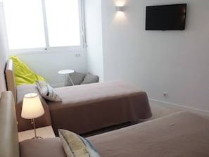 A room with two beds, a small table, a lamp, a TV, and a window.