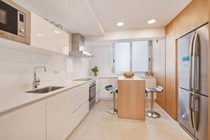 A modern kitchen with white cabinetry, stainless steel appliances, a central island with stools, and a window providing natural light.
