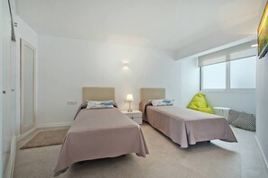 A hotel room with two beds, a nightstand, a lamp, a window, and a door. - Apartment 'Maina' with Sea View, Wi-Fi and Air Conditioning (Pollença)