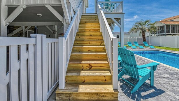 A wooden staircase leading to a pool area with turquoise chairs and a white fence. - Tranquil, Completely Renovated Three Bedroom Beach Home with a Private Pool! (Garden City Beach)