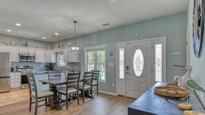 A spacious kitchen with a dining area, wooden flooring, and a large window. - Tranquil, Completely Renovated Three Bedroom Beach Home with a Private Pool! (Garden City Beach)
