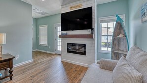 A living room with a fireplace, a television mounted above it, and a couch. - Tranquil, Completely Renovated Three Bedroom Beach Home with a Private Pool! (Garden City Beach)