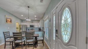 A dining area with a wooden table and chairs, a chandelier, and a large stained glass window. - Tranquil, Completely Renovated Three Bedroom Beach Home with a Private Pool! (Garden City Beach)