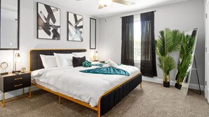 Une chambre moderne avec un lit, des tables de chevet, un ventilateur de plafond et de grandes fenêtres avec des rideaux.
