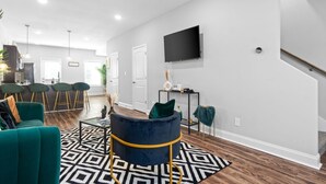 Un salon moderne avec un fauteuil bleu foncé, un tapis à motifs noir et blanc et un téléviseur à écran plat fixé au mur.