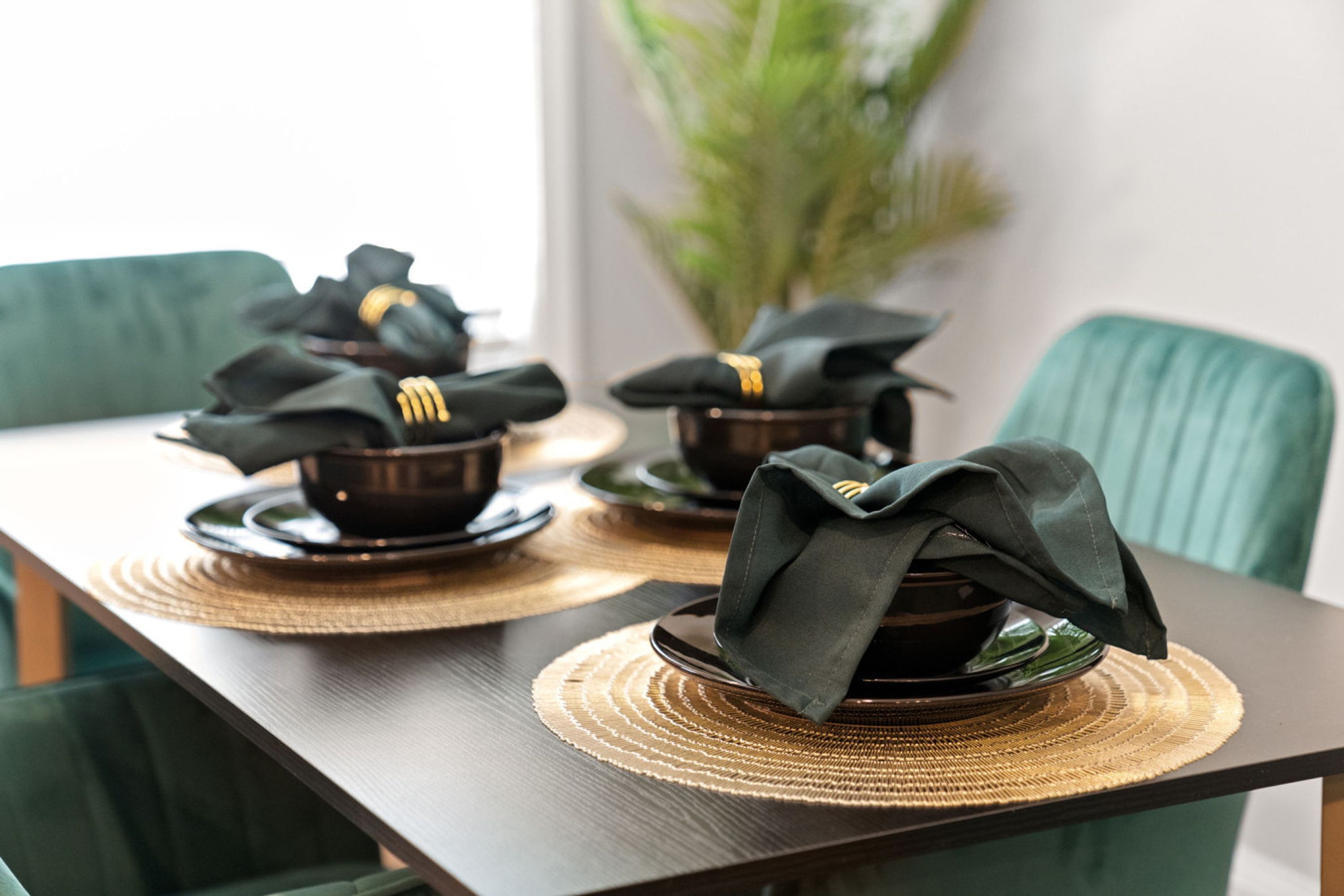 A dining table with black bowls and green napkins, set on a woven placemat.