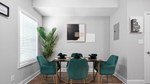 Un coin repas avec une table dressée pour quatre personnes, entourée de chaises turquoise aux pieds dorés.