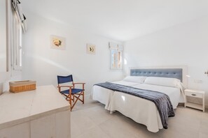 Ein Schlafzimmer mit Bett, Sessel, Nachttisch und Fenster.