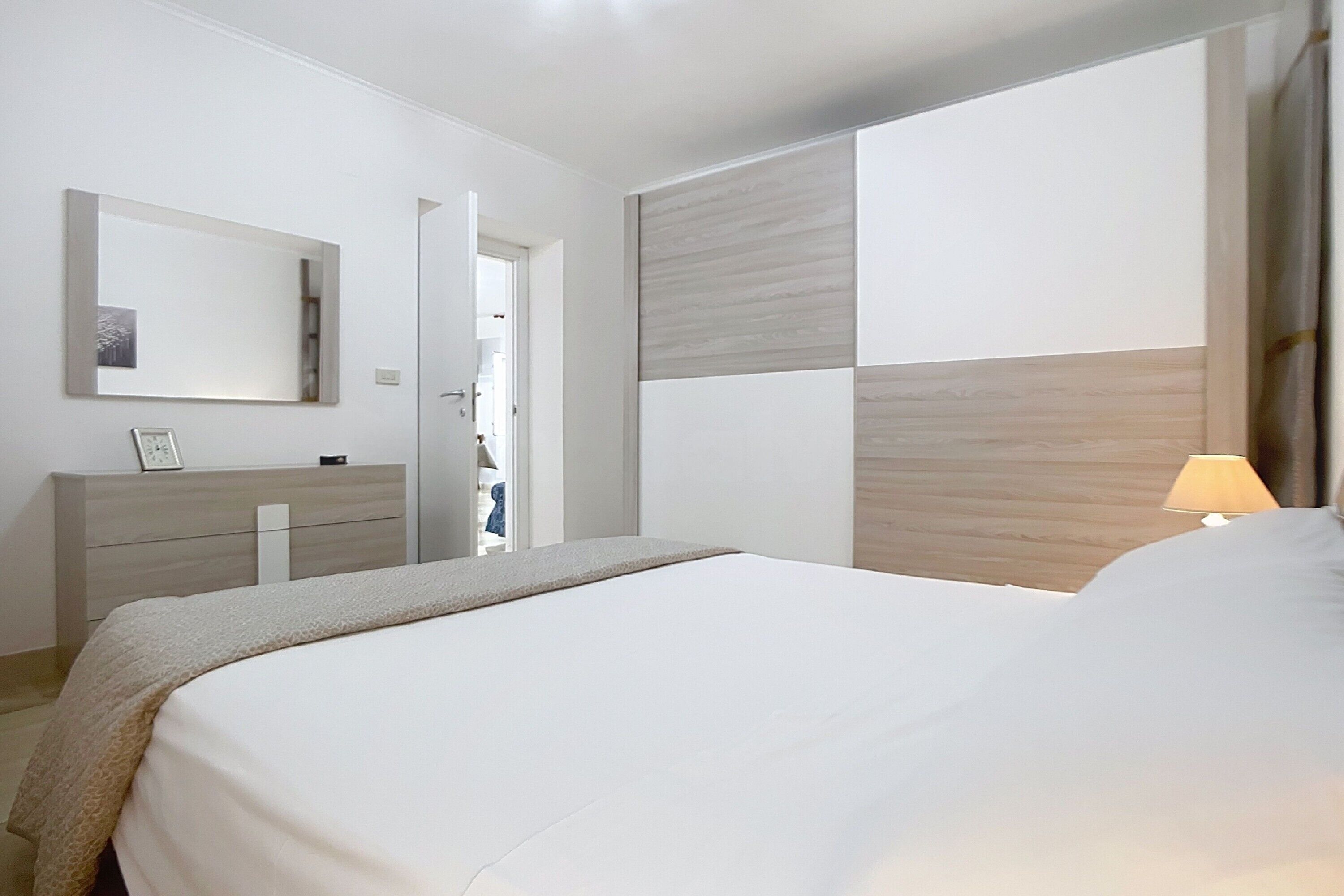 Een moderne slaapkamer met een bed, een dressoir, een spiegel en uitzicht op een gang.