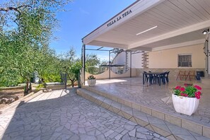 A covered outdoor area with a tiled floor, a seating area with chairs, and a potted plant with flowers. - Villa 'La Tesa' with Private Pool, Wi-Fi, and Air Conditioning (Madonna delle Grazie)