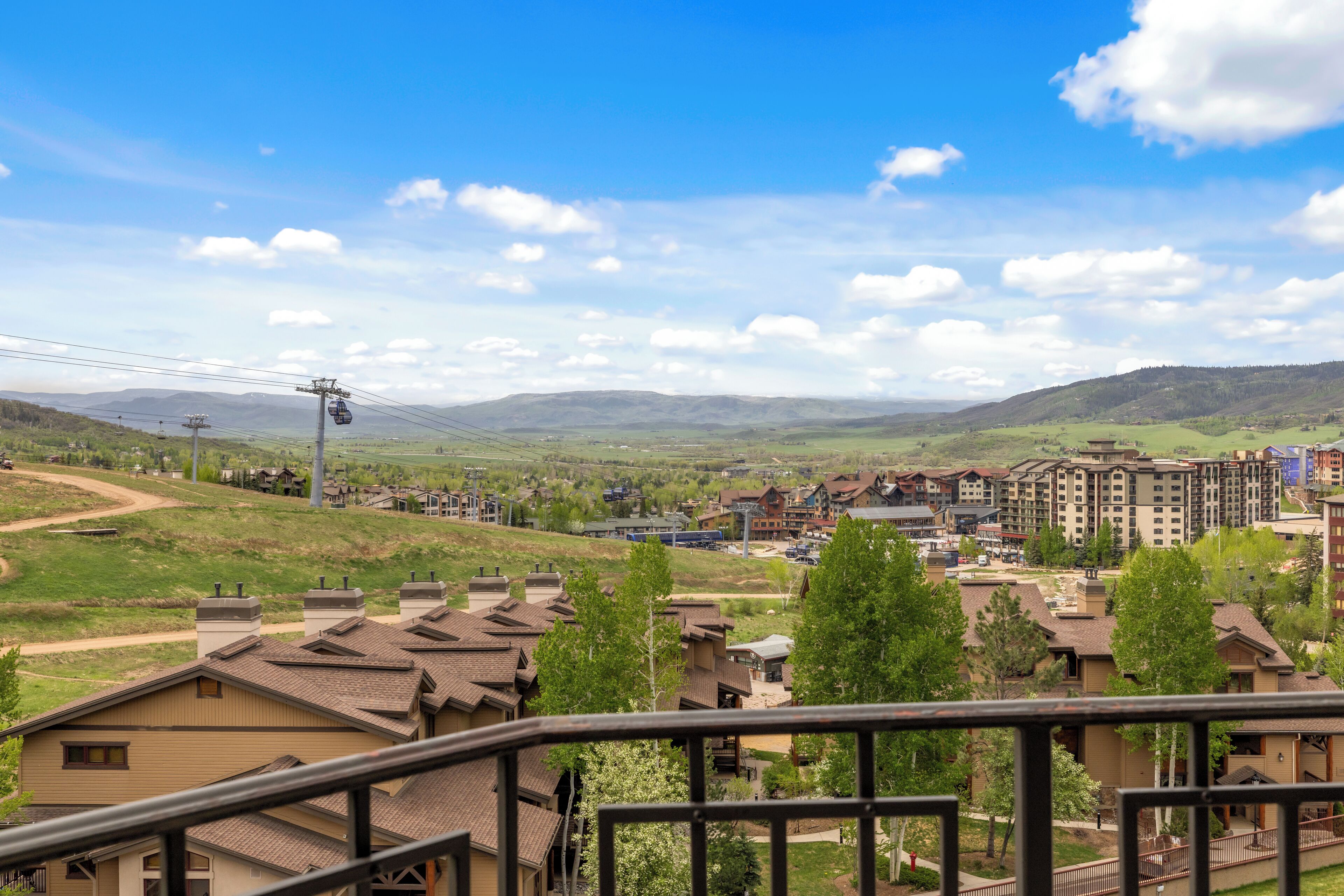 A residential area with a mix of single and multi-story houses, a ski lift, and a clear view of distant mountains.