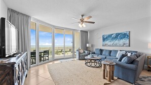 A spacious living room with a large sofa, a coffee table, and a view through a sliding glass door to the outdoors.