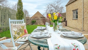 A table set for four with a floral tablecloth, a vase of flowers, and two glasses of water. - Country Cottage in the Heart of the Cotswolds (Cheltenham)