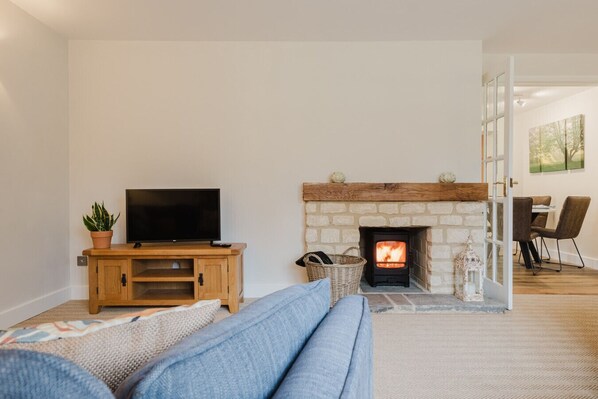 A living room with a stone fireplace, a television on a wooden stand, and a sofa. - Country Cottage in the Heart of the Cotswolds (Cheltenham)