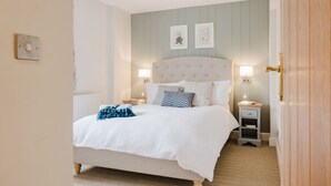 A bedroom with a bed, two bedside tables, a nightstand, a lamp, and a door. - Country Cottage in the Heart of the Cotswolds (Cheltenham)