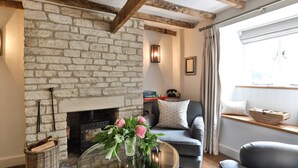 Un salon chaleureux avec une cheminée en pierre, un canapé confortable, une table basse en verre ornée de fleurs et une fenêtre avec des rideaux.