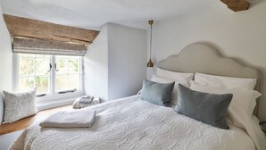 Une chambre avec un grand lit, une fenêtre offrant une belle vue, un luminaire suspendu et des poutres apparentes.