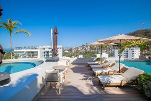A rooftop pool area with lounge chairs, a table, and umbrellas.