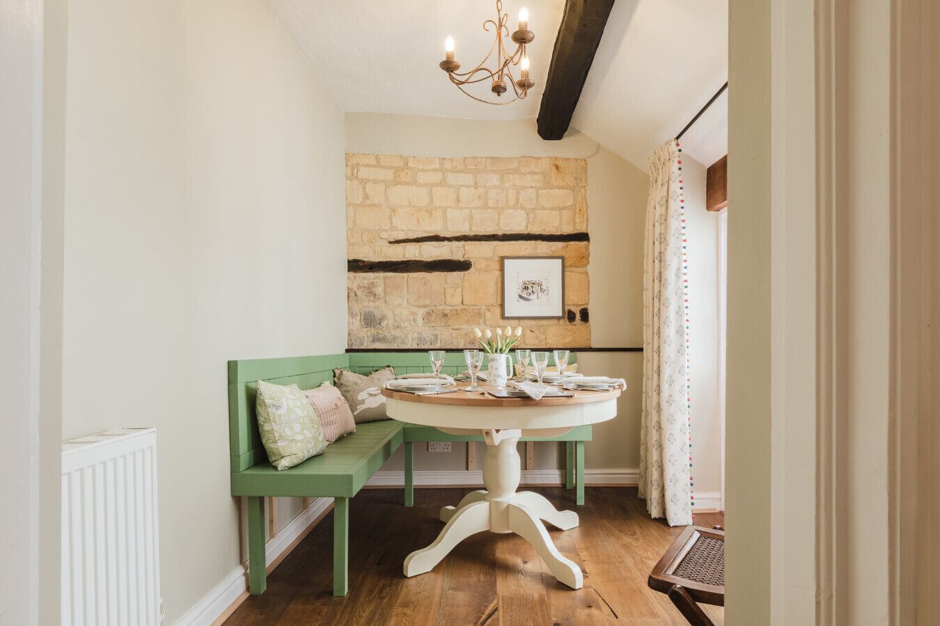 A cozy dining area with a stone wall, a green bench, and a round table set for four.