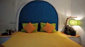 A bed with a yellow bedspread and two pillows, one green and one orange, in a room with a blue arched headboard and a wall-mounted lamp. - Bastar Birds Nest (Jagdalpur)