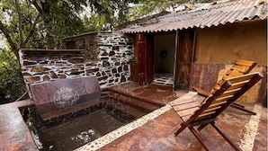 A stone-walled hot tub area with a wooden bench and a tiled walkway. - Bastar Birds Nest (Jagdalpur)