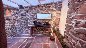 A stone-walled interior with a stone bench, a mounted television, and a fire feature. - Bastar Birds Nest (Jagdalpur)