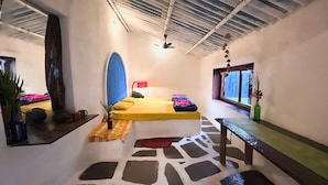 A compact room with a bed, a small table, a bench, a window, and a ceiling fan. - Bastar Birds Nest (Jagdalpur)