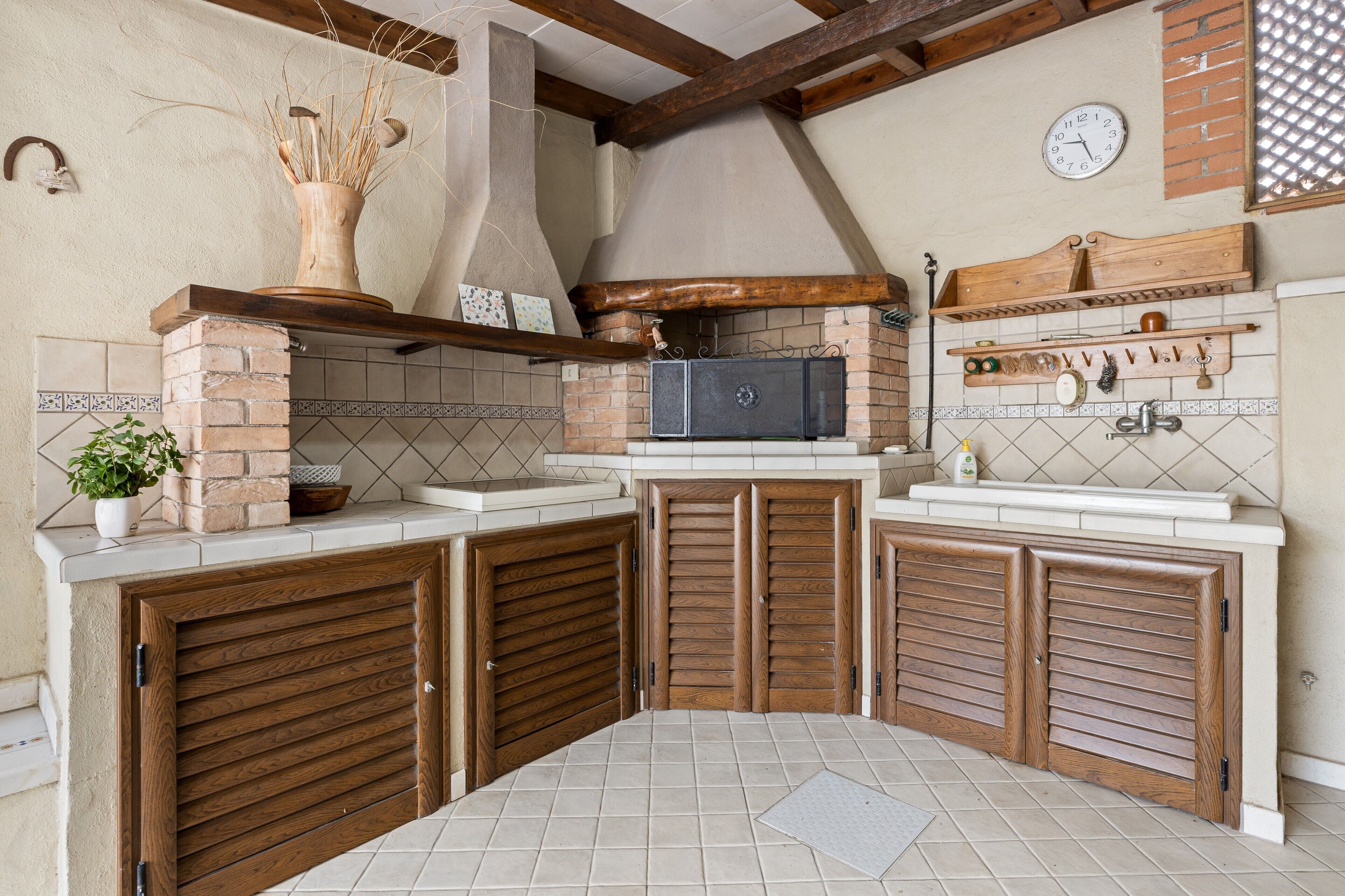 Una cocina con pared de ladrillo, armarios de madera, un reloj y suelo de baldosas.