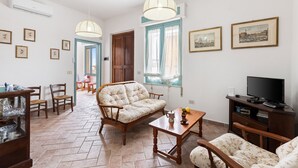 Un salon avec un canapé, des fauteuils, une table basse, un téléviseur et des tableaux encadrés au mur.