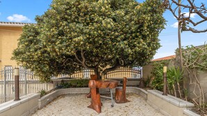 Une cour avec un grand arbre, un banc en bois et un sol carrelé.